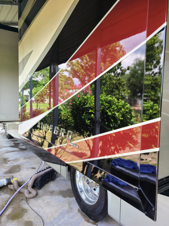 Glossy red Allegro motorhome reflecting the surrounding trees
