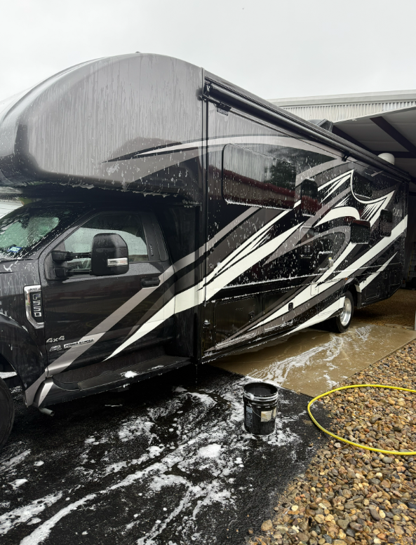 Soap suds covering a black Class C motorhome during a wash